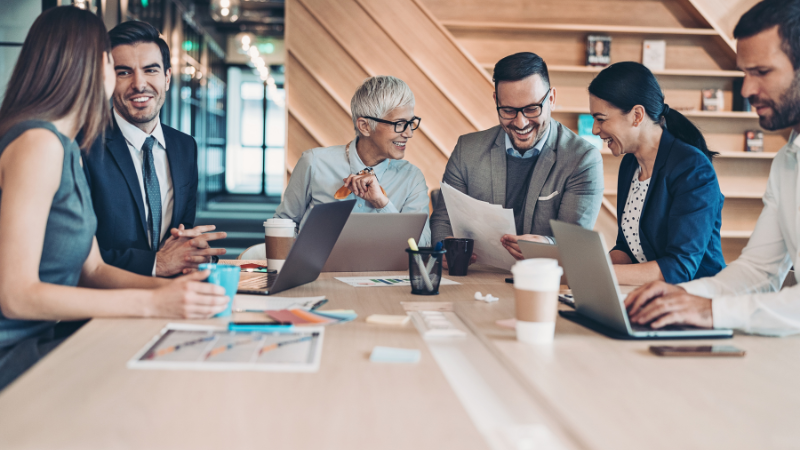 A team of business professionals collaborating over laptops and documents in a modern office, representing thought leadership content seeding in niche communities — a strategy that drives authority and rankings for Clicks Gorill's clients.