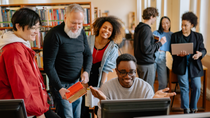 A diverse group of people collaborating around a computer in a library setting, representing community-driven content seeding — a strategy championed by Clicks Gorill to build trust and organic visibility.